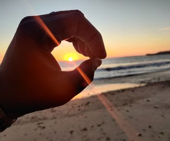 Midsection of person holding sun over sea during sunset