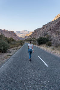 Rear view of woman walking on road against clear sky