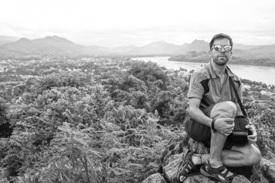 Full length of man sitting on landscape against mountains