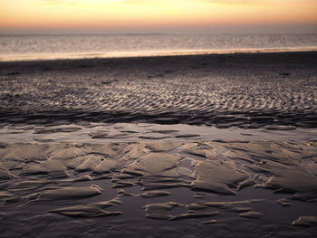 Surface level of beach against sky during sunset