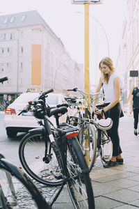 Full length of young entrepreneur locking bicycle on sidewalk in city