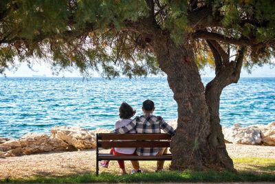 Rear view of people sitting on bench by sea