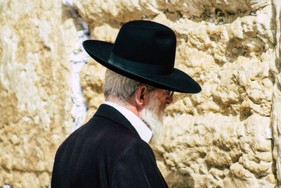 Portrait of man wearing hat standing against stone wall