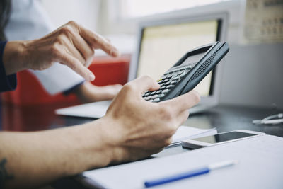 Cropped hand of teacher pointing at young male student holding calculator in classroom