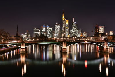 Illuminated bridge over river by buildings against sky at night