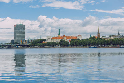 View of buildings by river against cloudy sky