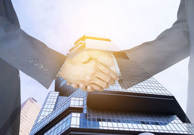 Digital composite image of business people giving handshake against building