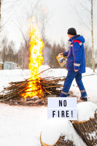 A man in a blue uniform pours gasoline from a canister into the fire. 