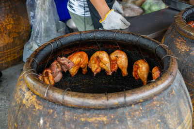 Barbecue chicken drum sticks and thighs hanging in a ceramic pot over charcoal in an outdoor kitchen