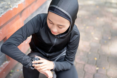 Midsection of young woman holding camera while standing against wall