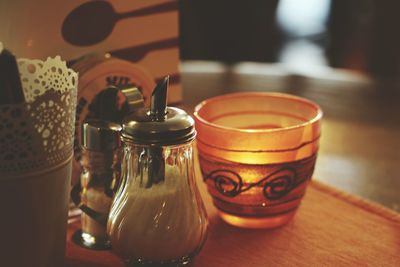 Close-up of salt and pepper shaker with lit candle on table