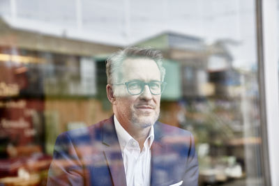 Portrait of confident mature businessman behind windowpane