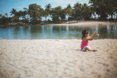 Side view of girl playing with sand while sitting at lakeshore