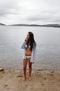 Portrait of young woman standing at beach against sky