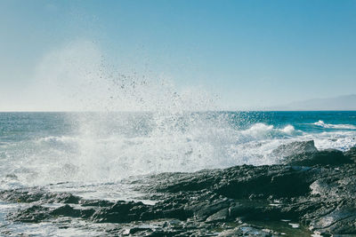 Sea waves splashing on rocks against clear sky