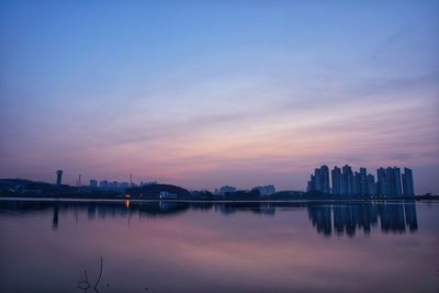 Scenic view of lake by buildings against sky at sunrise