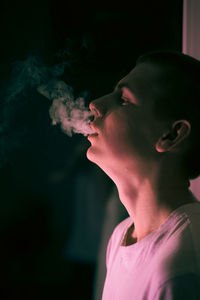 Close-up portrait of young man smoking against black background