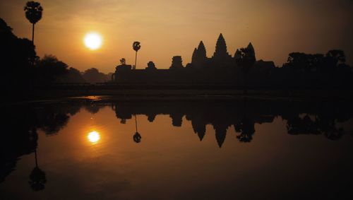 Reflection of silhouette angkor wat on calm lake against sky during sunset