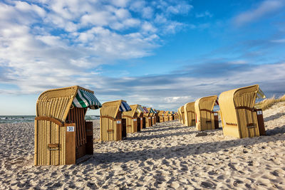 Hooded chairs at sandy beach against cloudy sky