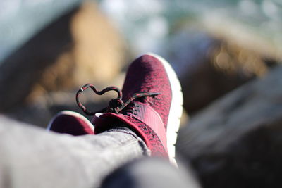 Low section of person wearing shoe while sitting on rock at beach