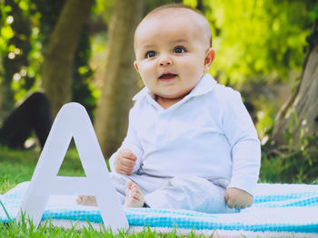 Baby boy looking away while sitting on blanket at park