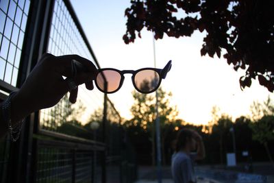 Close-up of silhouette hand holding sunglasses against sky