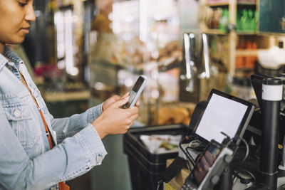 Woman using smart phone while scanning qr code for payment at store checkout