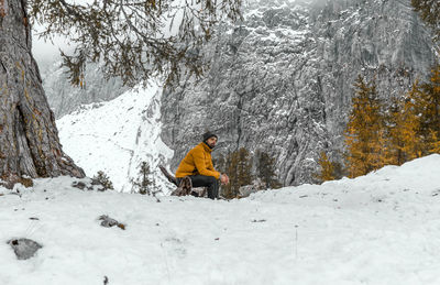 Young man sitting under tree in amazing mountains in winter.