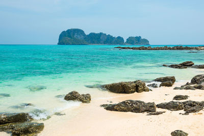 Tropical sea landscape with rocks at sand beach and rocky island at horizon