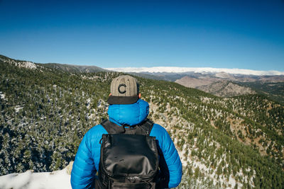 Rear view of man looking at mountains against blue sky