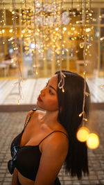 Portrait of young woman looking at illuminated shop