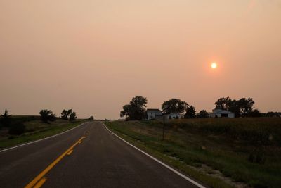 Road amidst field against sky during sunset