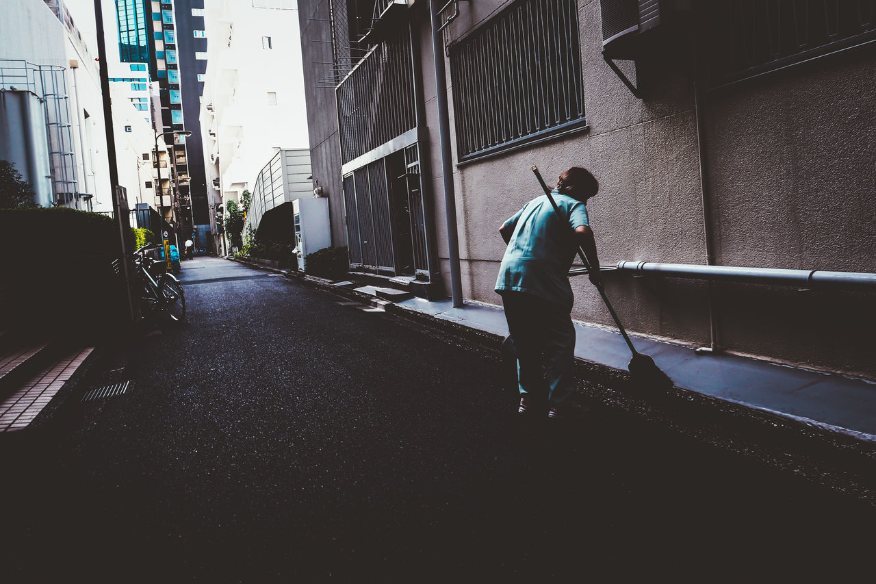 FULL LENGTH REAR VIEW OF MAN WALKING ON STREET AMIDST BUILDINGS