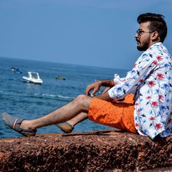 Side view of young man looking at sea against sky