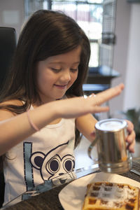 Girl sprinkling sugar on waffle while sitting at table in home