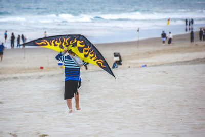 Rear view of boy holding kite while standing at beach