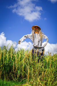 Woman standing by plants on field against sky