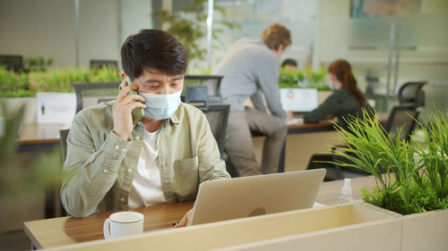 Businessman talking on phone while wearing mask at office