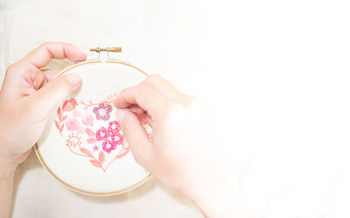 Female hand holding wood embroidery frame and needle working on flower pattern stitching.