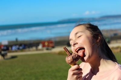 Smiling girl licking ice cream on field during sunny day