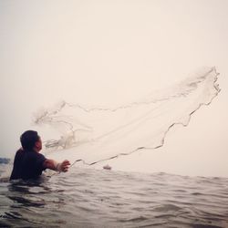 Fisherman casting fishing net in lake against sky
