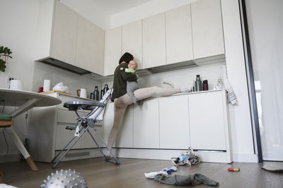 Flexible mother with leg stretched on kitchen counter carrying son at home