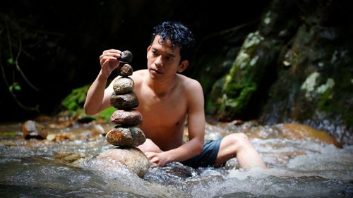 Shirtless young man stacking stone on river