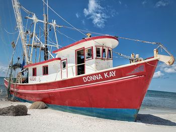 Red fishing boat moored at port against sky