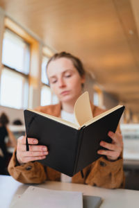 Soft focus of young woman checking notes in planner while sitting at table and studying in university library