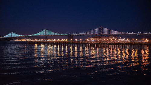 Illuminated bridge over river against sky at night