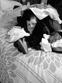 Portrait of smiling boy covered with clothes on bed at home