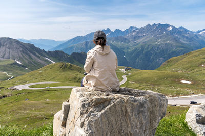 Rear view of woman sitting against mountains on rock