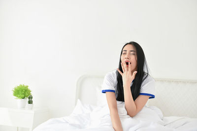 Young woman yawning against wall on bed at home