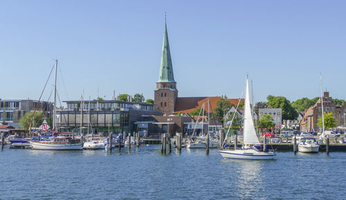 Sailboats in river by buildings against sky